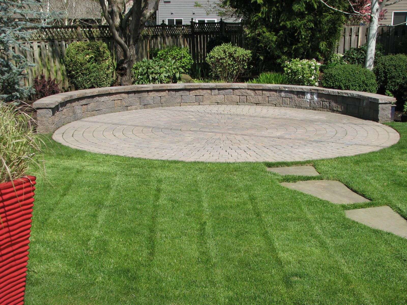 A circular paver patio and seating wall create a ...